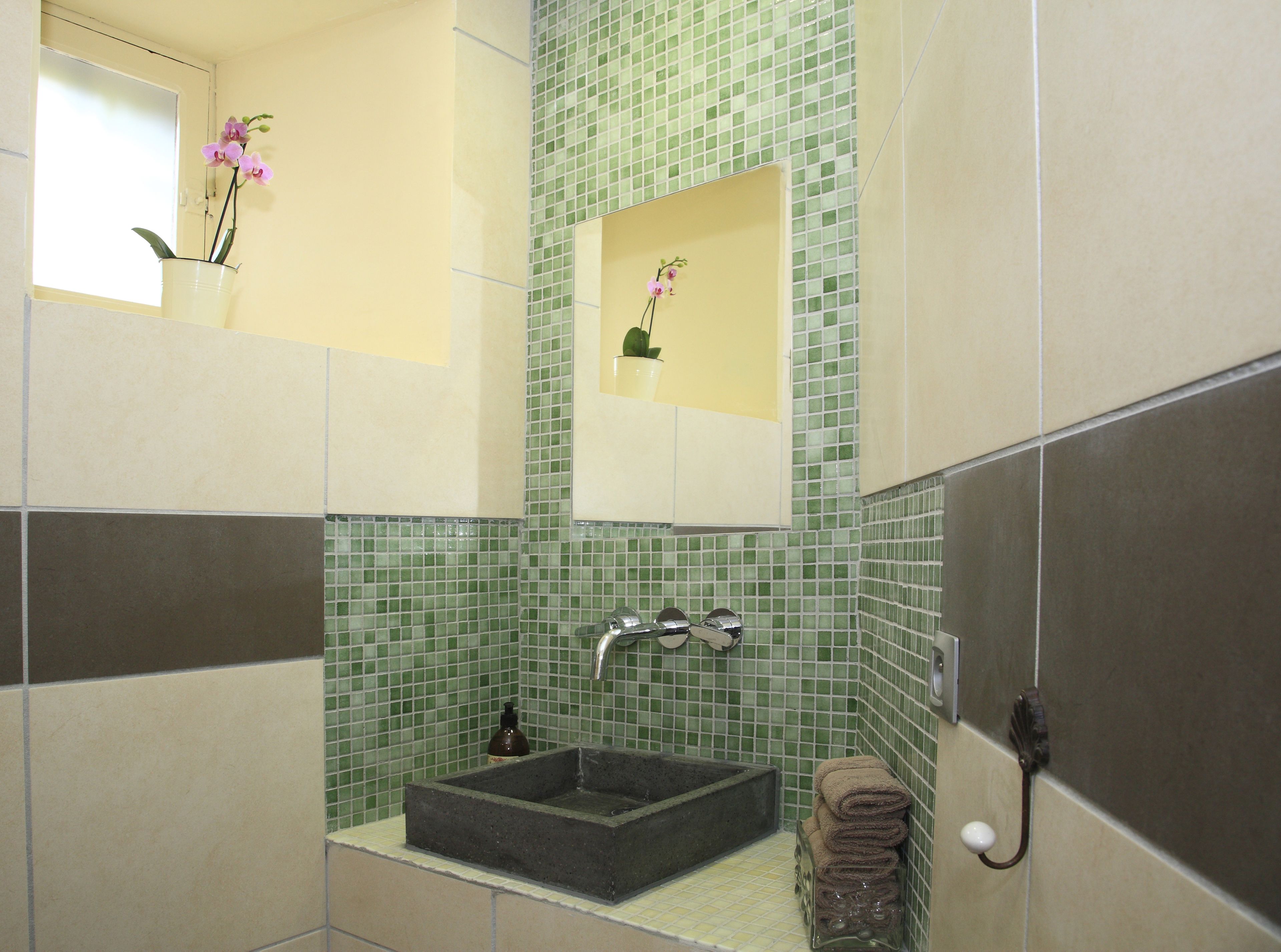 A bathroom with a rectangular sink, a mirror, and a green mosaic tile wall.
