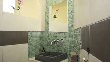 A bathroom with a rectangular sink, a mirror, and a green mosaic tile wall.