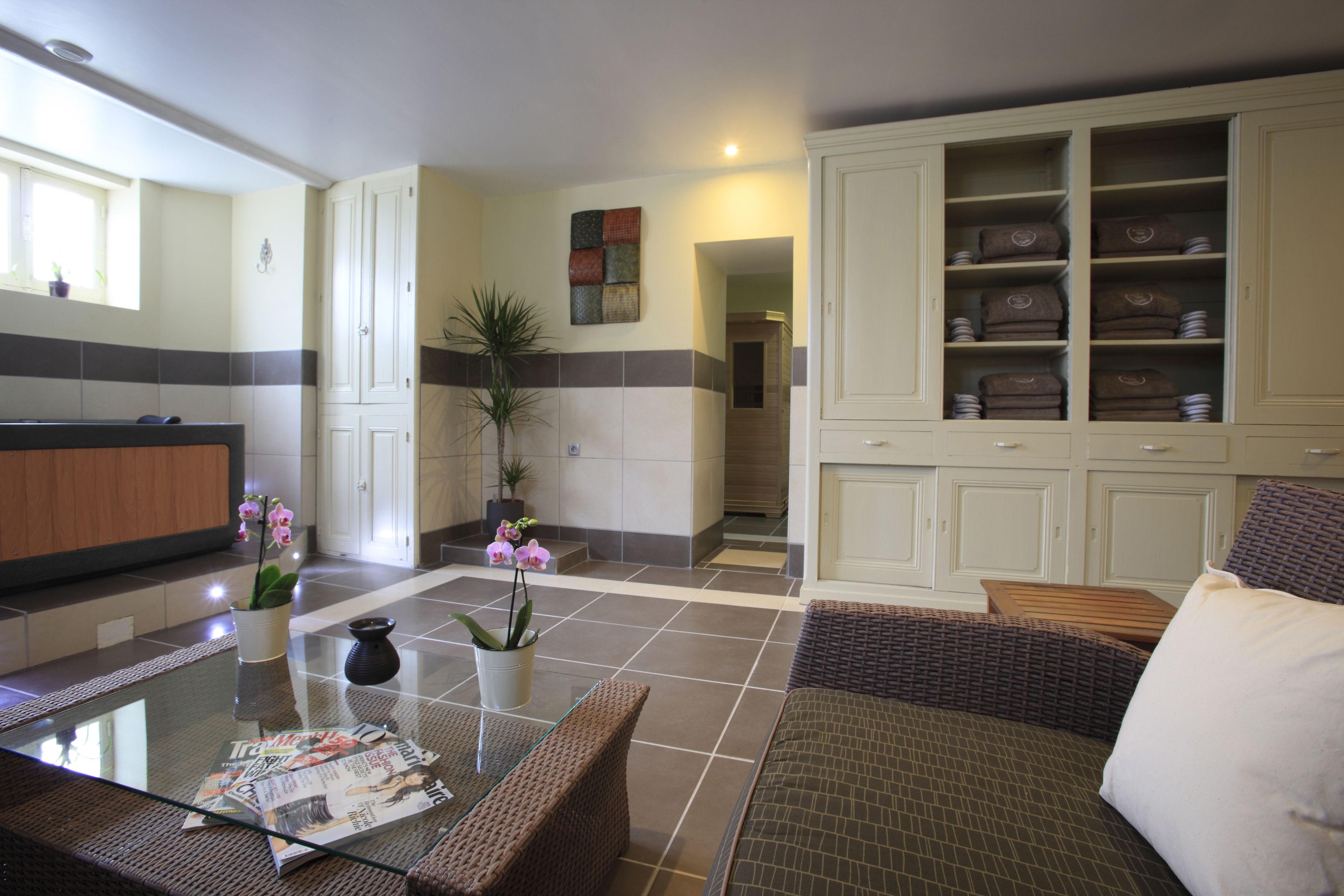 Une chambre d’hôtel moderne avec une table basse en verre, des meubles en osier, une plante en pot et une grande armoire avec des étagères.