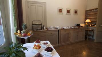 A breakfast buffet with various fruits and a coffee station in a well-lit kitchen area.