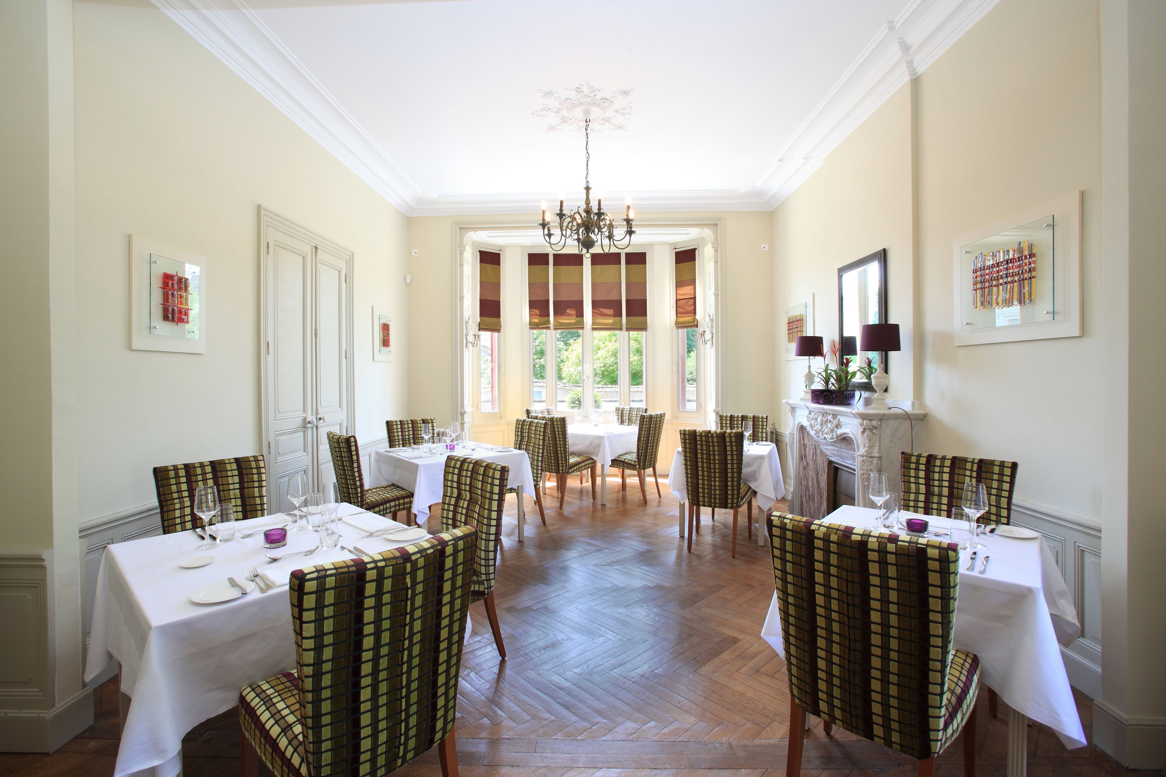 A dining room with multiple tables and chairs, a chandelier, and framed artwork on the walls.