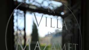 Una puerta de cristal con la inscripción "LA VILLA DI MAZAMET" y vista a un jardín.
