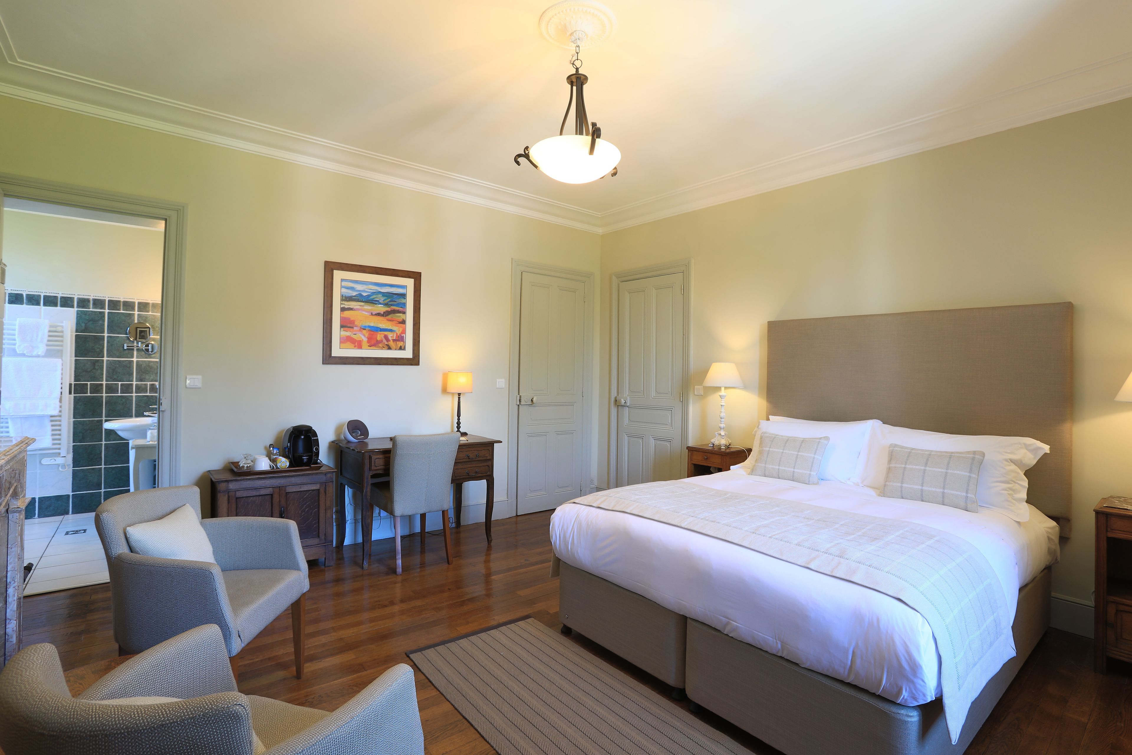 Une chambre d’hôtel avec un grand lit, un bureau avec une chaise, une petite table avec une lampe et un tableau au mur.
