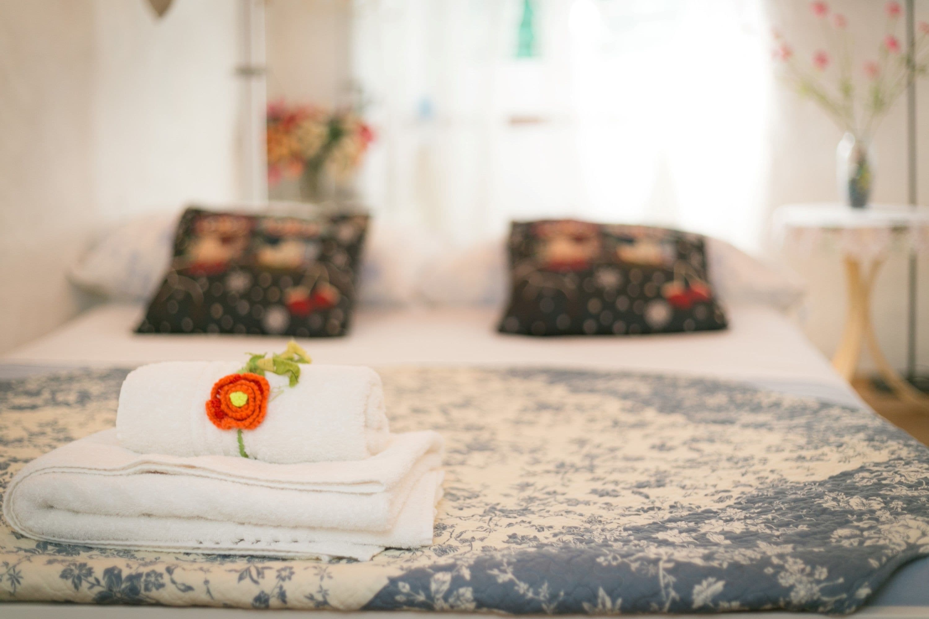 Una cama bien tendida con una colcha de estampado floral, una toalla blanca doblada con una flor roja y almohadas a juego con diseño floral.