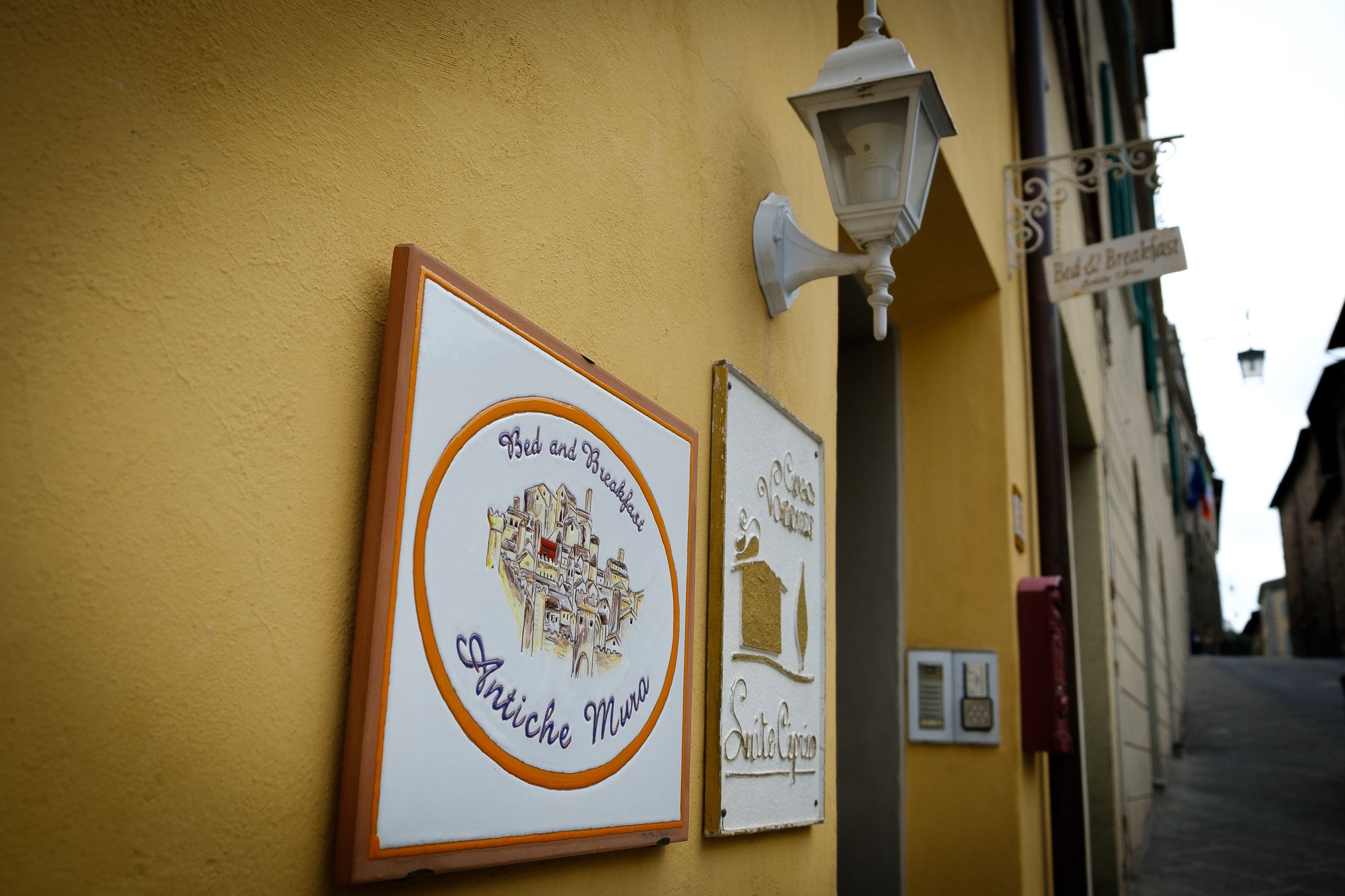 Dos carteles enmarcados sobre una pared amarilla, uno anuncia un hospedaje y desayuno y el otro una cafetería y panadería.