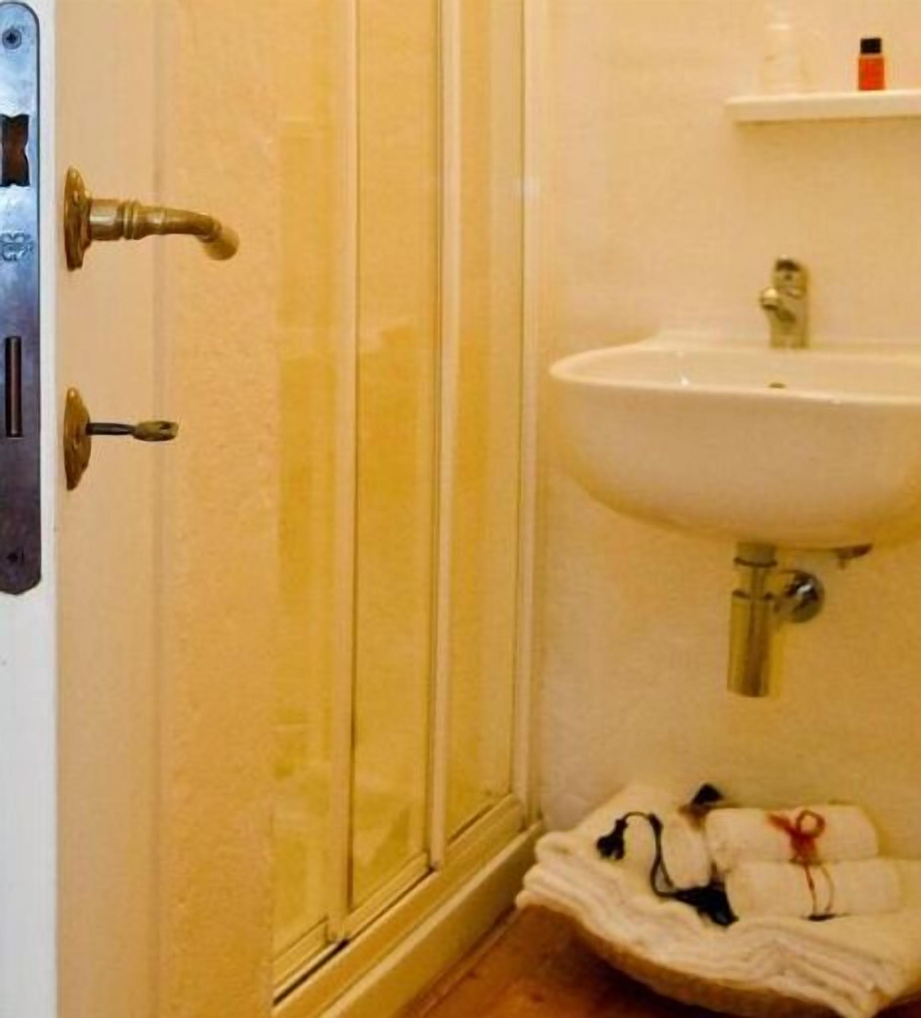 Et badeværelse med en hvid vask, en glasbrugedør og et håndklædetørrestativ med håndklæder.