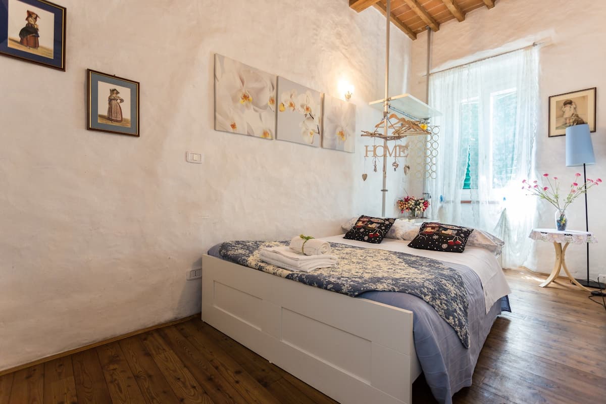 Un dormitorio con cama, decoración en la pared, una lámpara colgante y una ventana con cortinas.