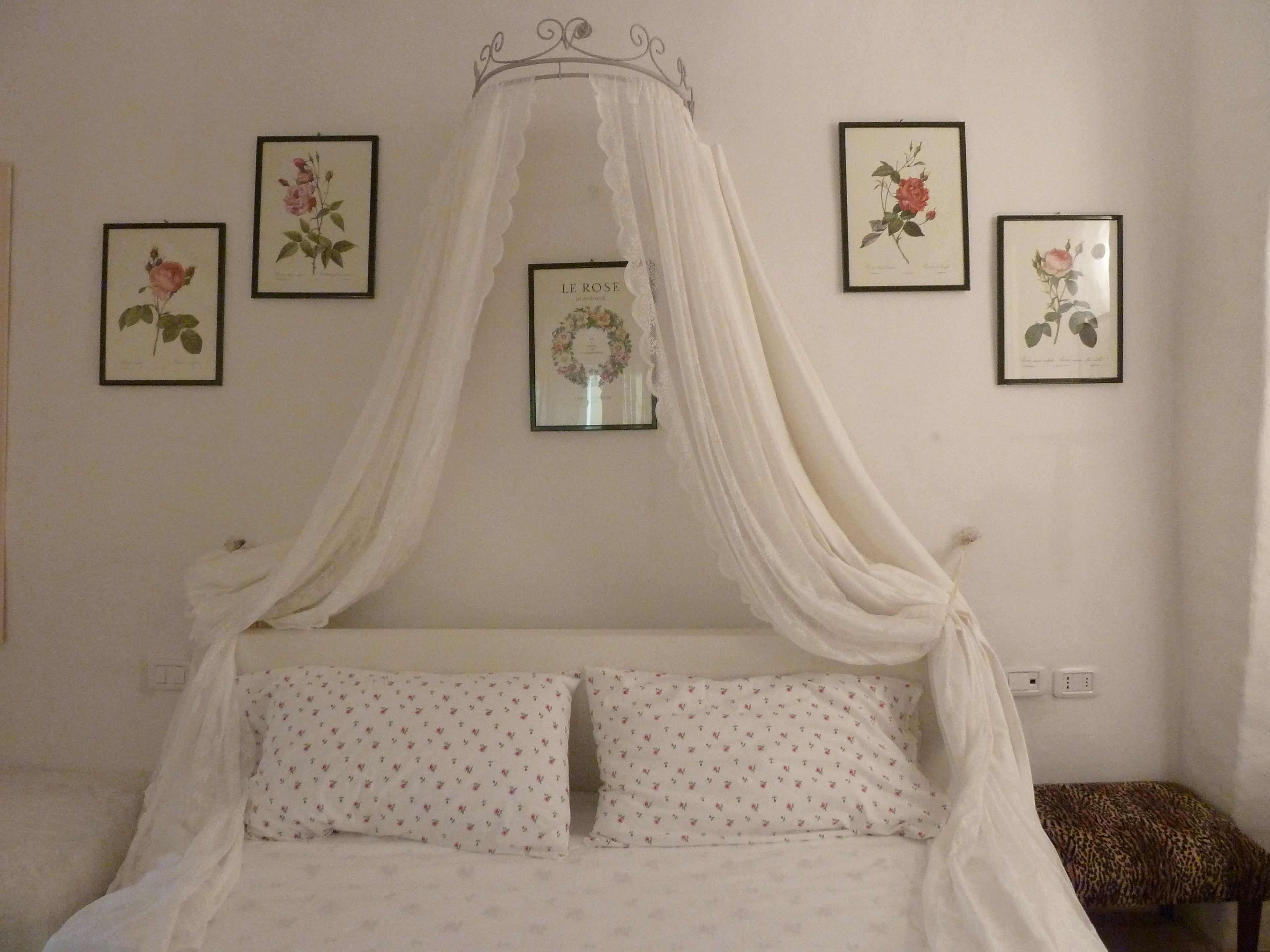 A bedroom with a canopy bed, floral wall art, and a leopard print bench.