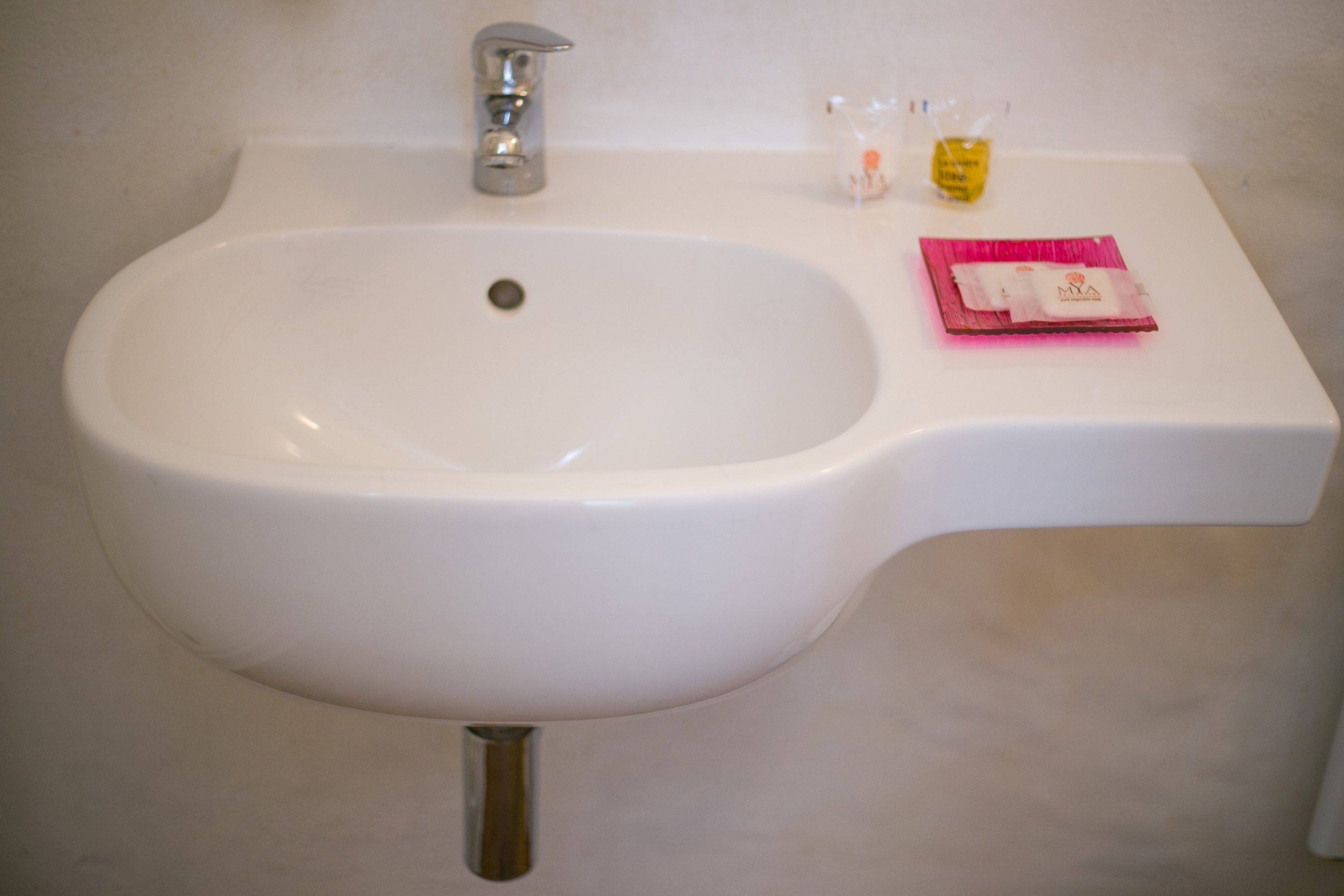 A white bathroom sink with a silver faucet, a small bottle of soap, and a pink packet of tissues on the counter.