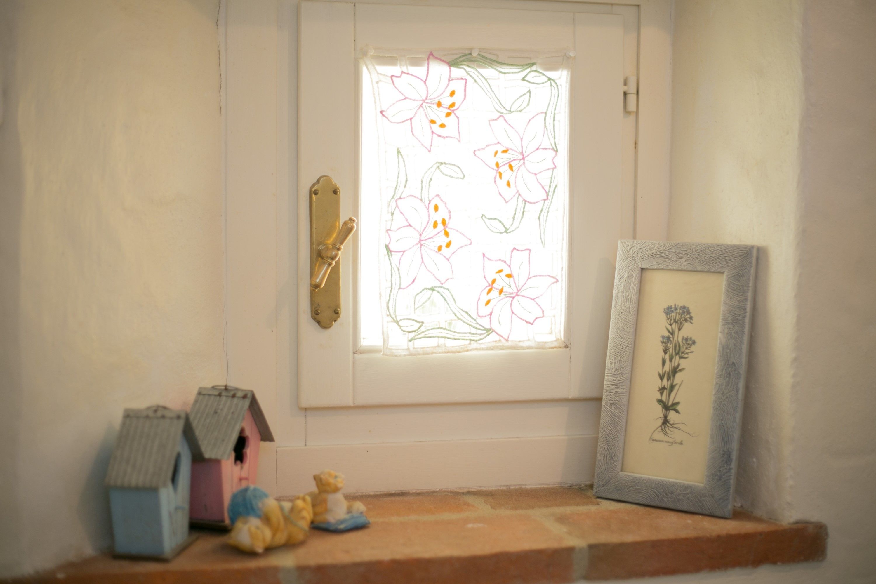 A white door with a window featuring floral designs, a small framed botanical illustration, and two birdhouses on a brick ledge.