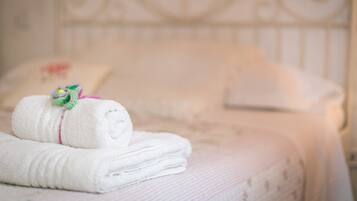 A neatly folded white towel with a decorative flower, placed on a bed with a floral-patterned bedspread.