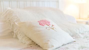 Un lit bien fait, recouvert d’une couvre-lit en dentelle et agrémenté d’un coussin orné de broderies florales.