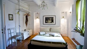 A bedroom with a bed, a chair, a bedside table, a hanging plant, and a picture on the wall. - Antiche Mura (Arezzo)