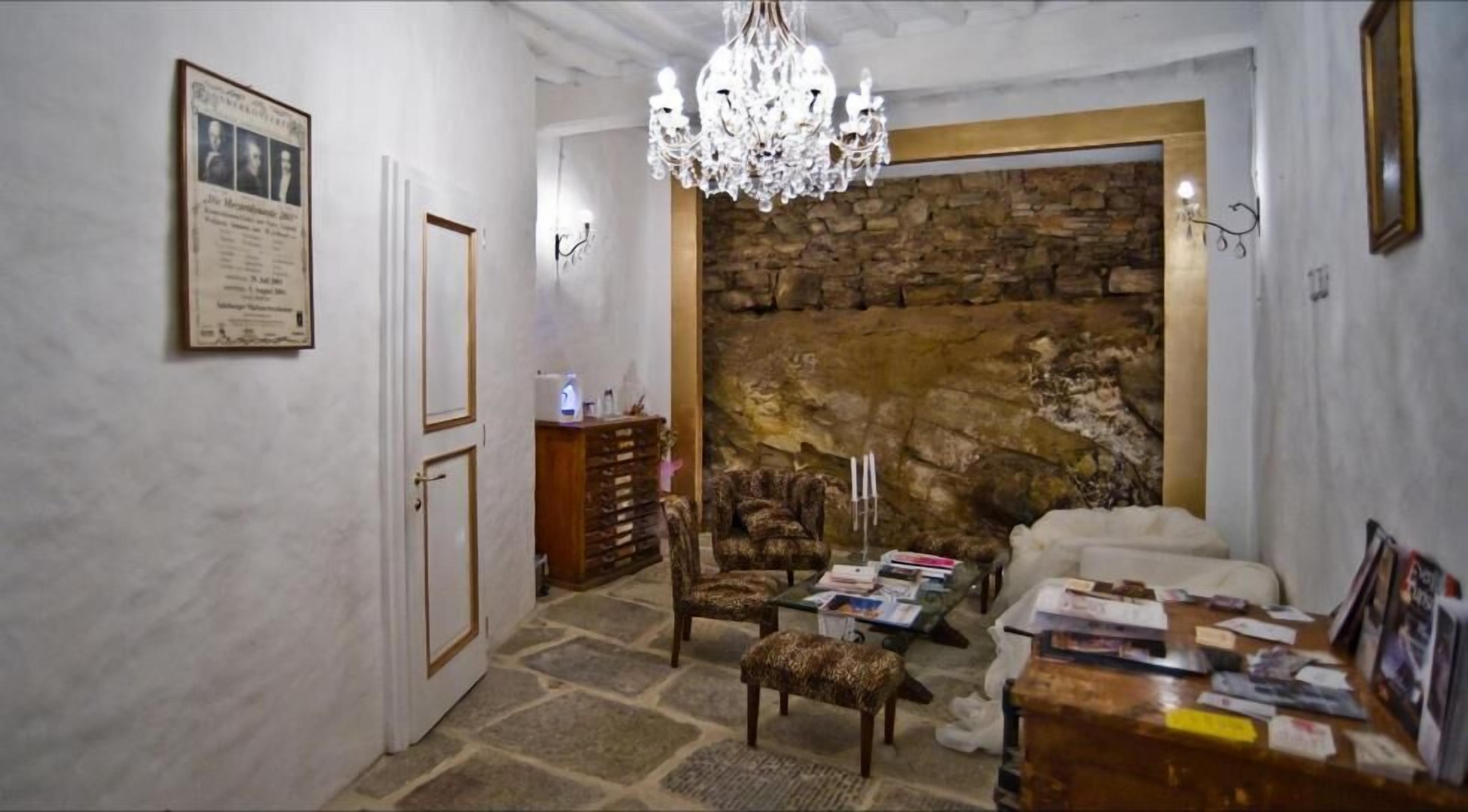 A room with a stone wall, a chandelier, a wooden cabinet, and a sofa.