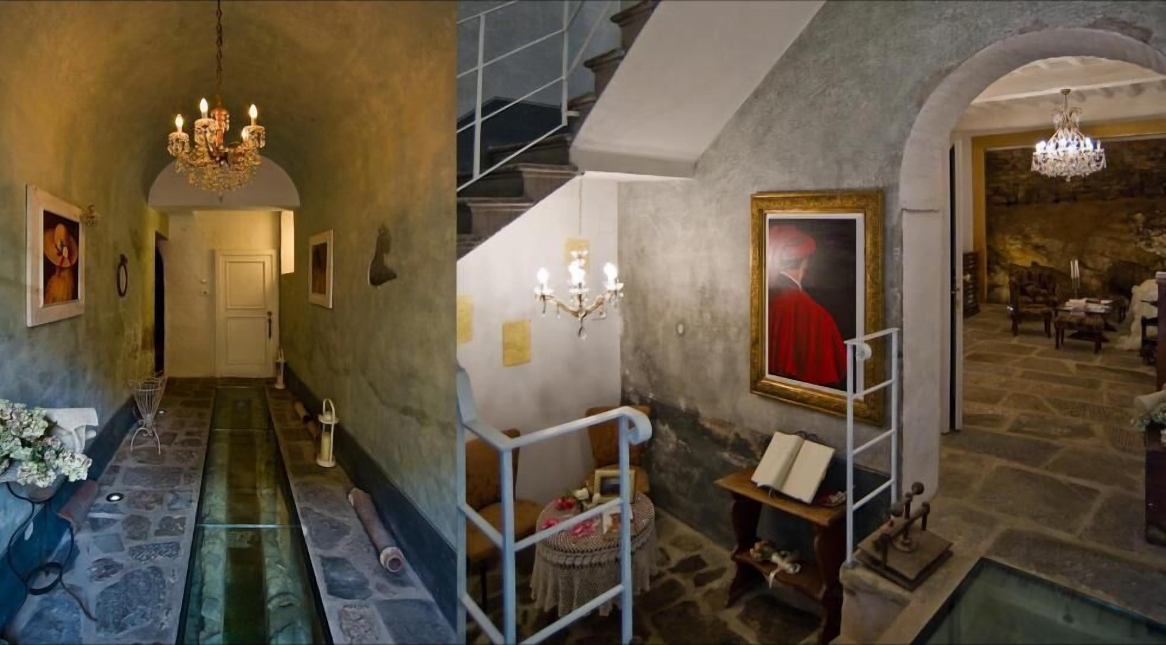 A grand staircase with a chandelier, a framed painting, and a stone floor.