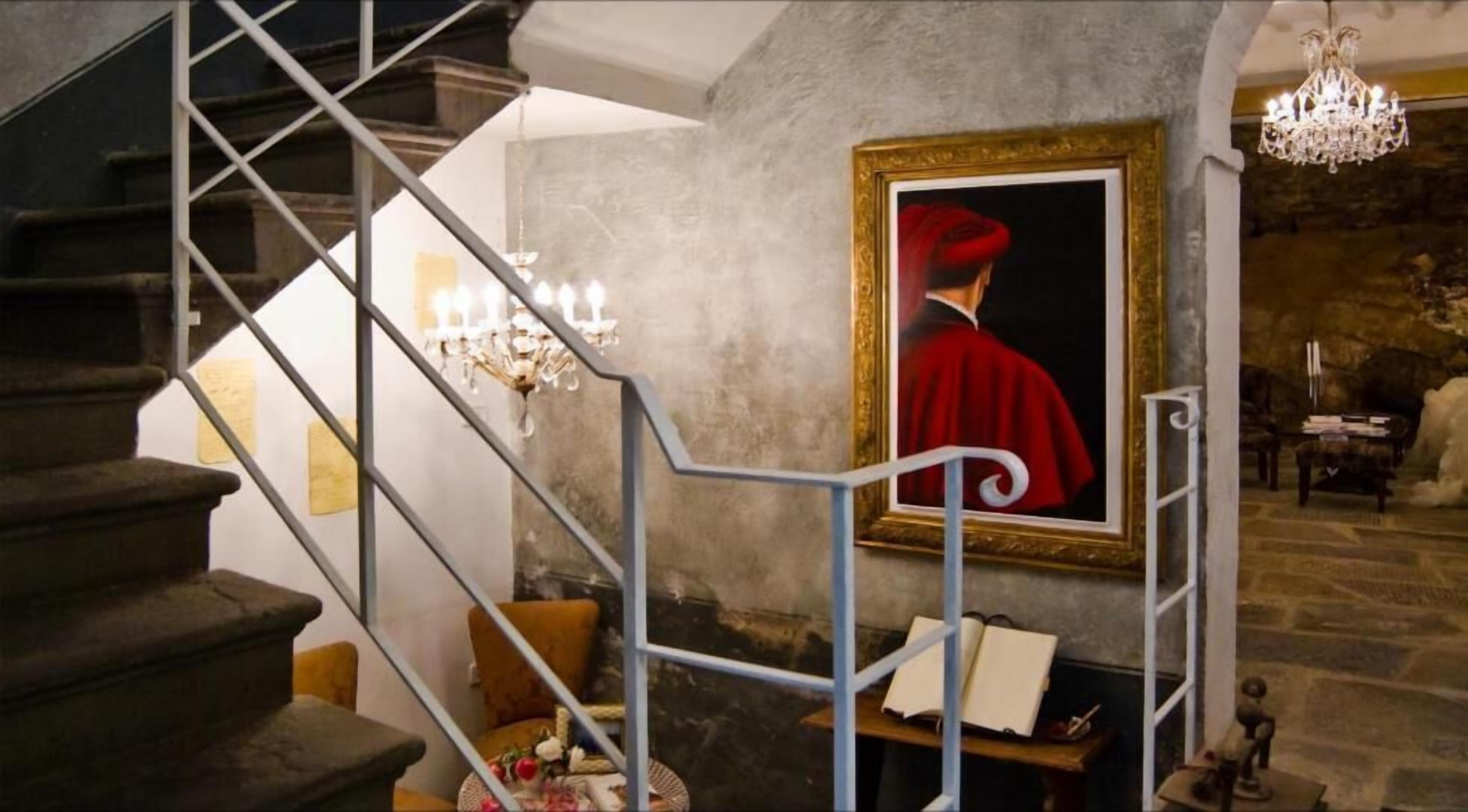 Een trap met een metalen leuning die leidt naar een kamer met een groot schilderij in een lijst, een kroonluchter en een stenen muur.