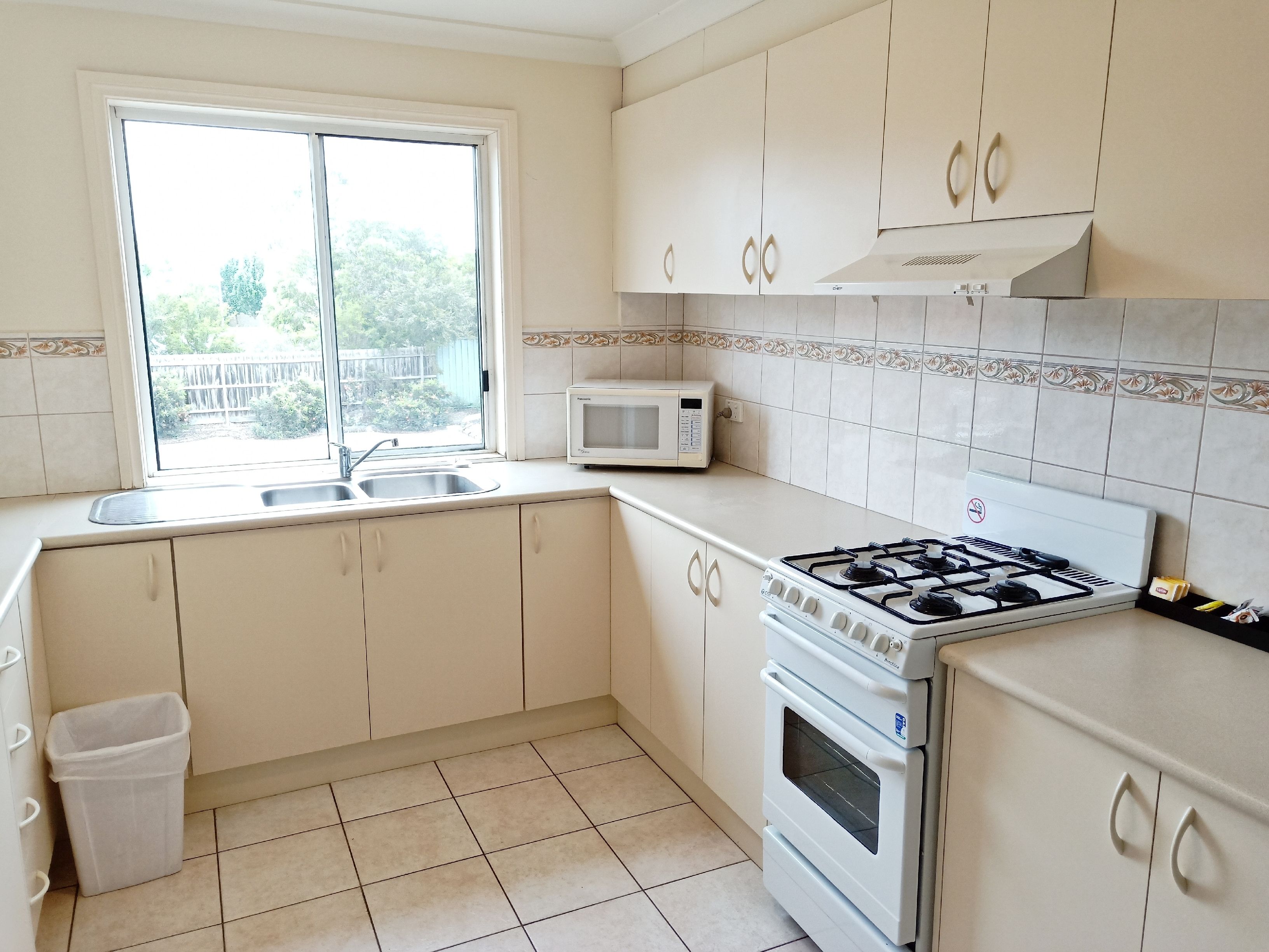 Una cocina con armarios blancos, estufa a gas, microondas y ventana con vistas al exterior.
