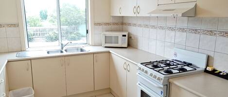 Una cocina con armarios blancos, estufa a gas, microondas y ventana con vistas al exterior.