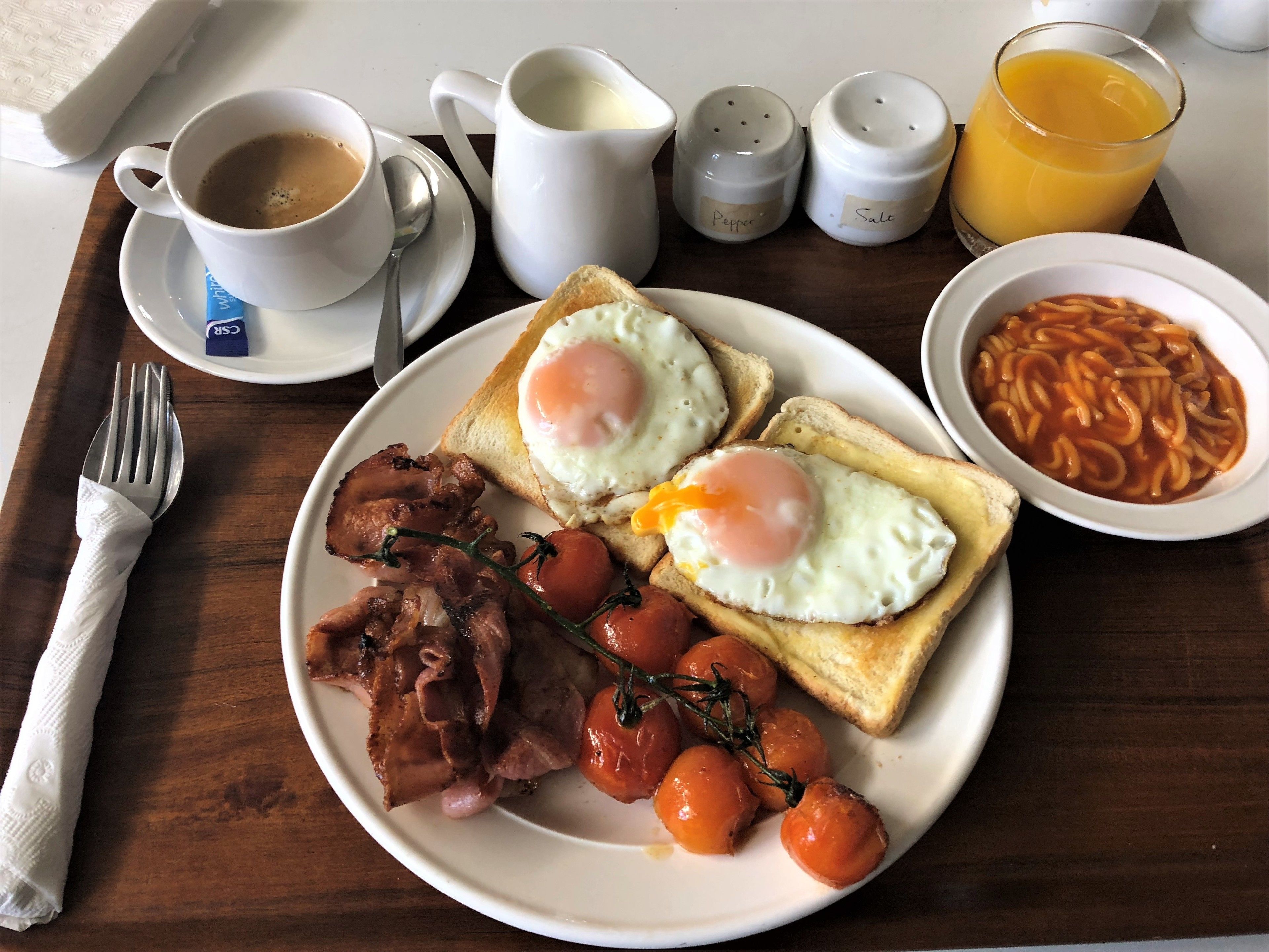 En morgenmadstallerken med æg, bacon, tomater og bønner.