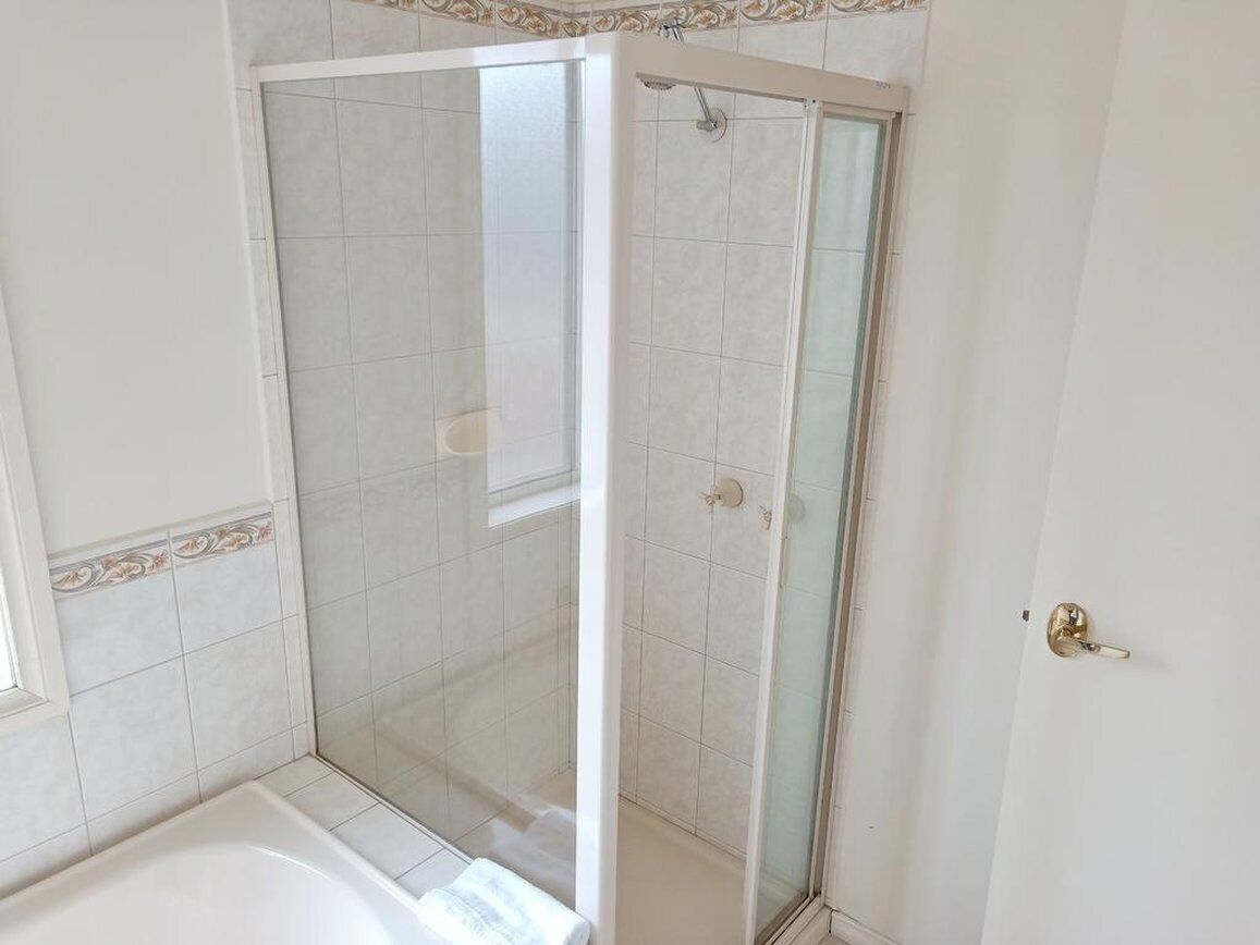 A bathroom with a glass-enclosed shower, a bathtub, and a door with a gold handle.