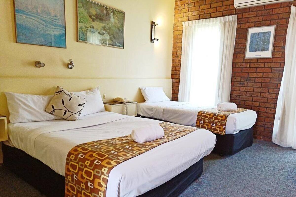 A hotel room with two beds, each with a patterned bedspread, a nightstand, and a telephone.