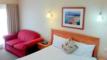 A hotel room with a bed, a red armchair, a bedside table with a phone, and two wall-mounted lamps.