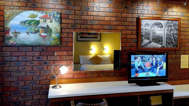 A hotel room with a brick wall, a television, a mirror, and a lamp. - Glen Inn (Glen Waverley)