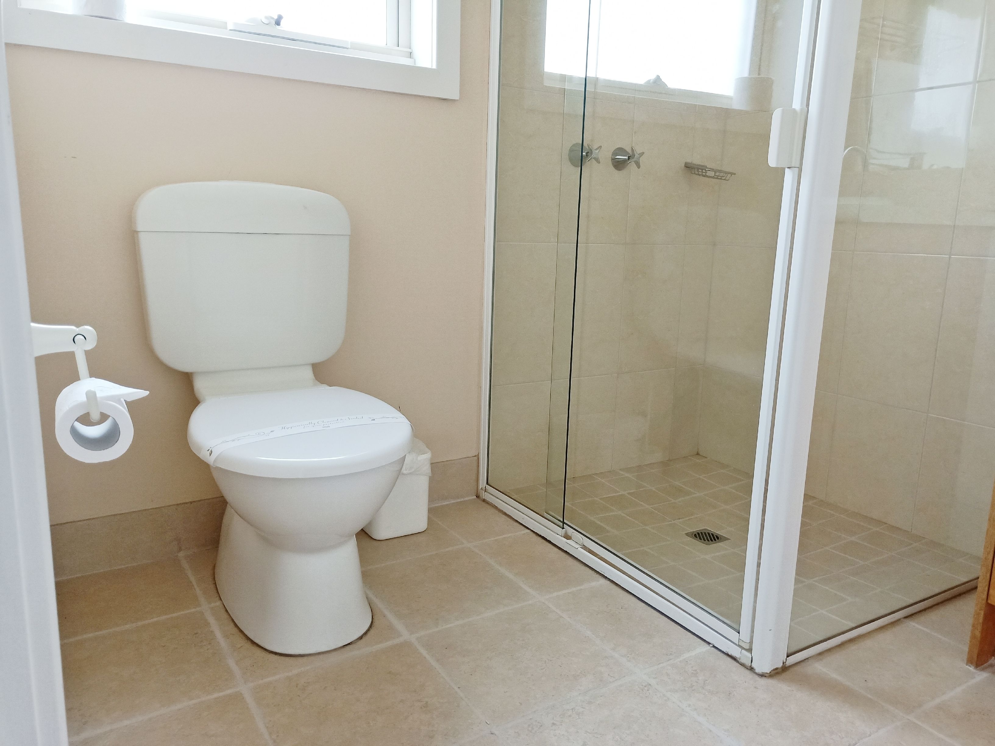 Une salle de bain avec des toilettes, une douche à parois de verre et un carrelage beige.