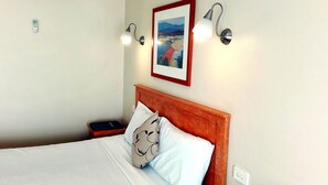 A neatly made bed with a wooden headboard, a bedside table with a book, and wall-mounted lights. - Glen Inn (Glen Waverley)
