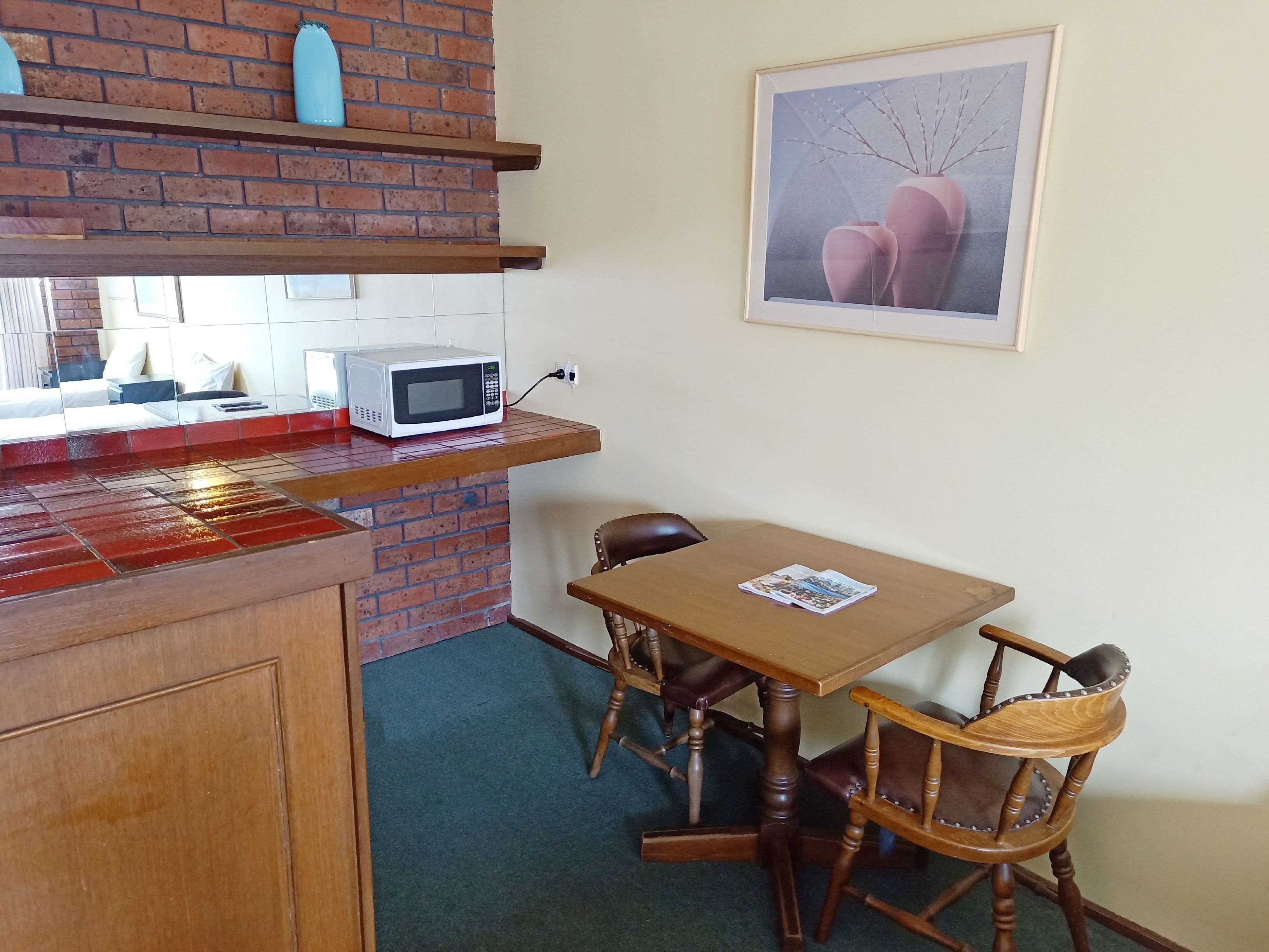 Une cuisine avec un four à micro-ondes posé sur une étagère, une table en bois et une chaise.