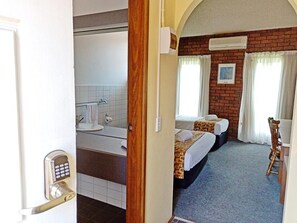 A hotel room with a bathroom, two beds, a desk, and a chair.