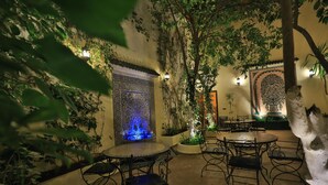 An indoor courtyard with a fountain, tables, chairs, and decorative walls. - Riad Jardin Chrifa (Fes)