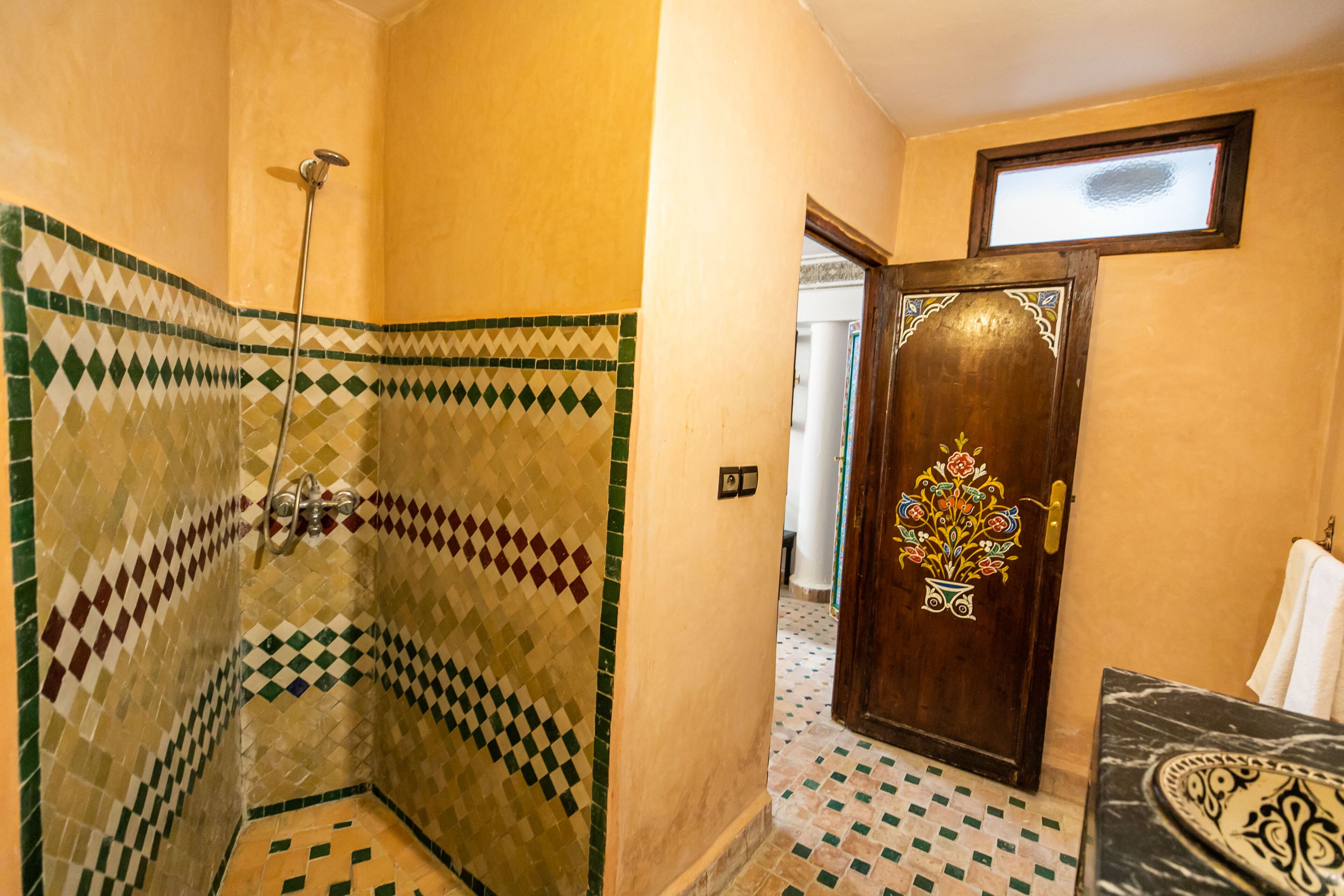 A bathroom with a shower, a door with a floral design, and a patterned floor.