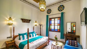 A room with a four-poster bed, a small round table with a vase, a wooden chair, and a mirror on the wall. - Riad Jardin Chrifa (Fes)