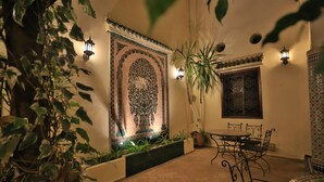 A courtyard with a decorative wall, potted plants, a table with chairs, and wall-mounted lights. - Riad Jardin Chrifa (Fes)