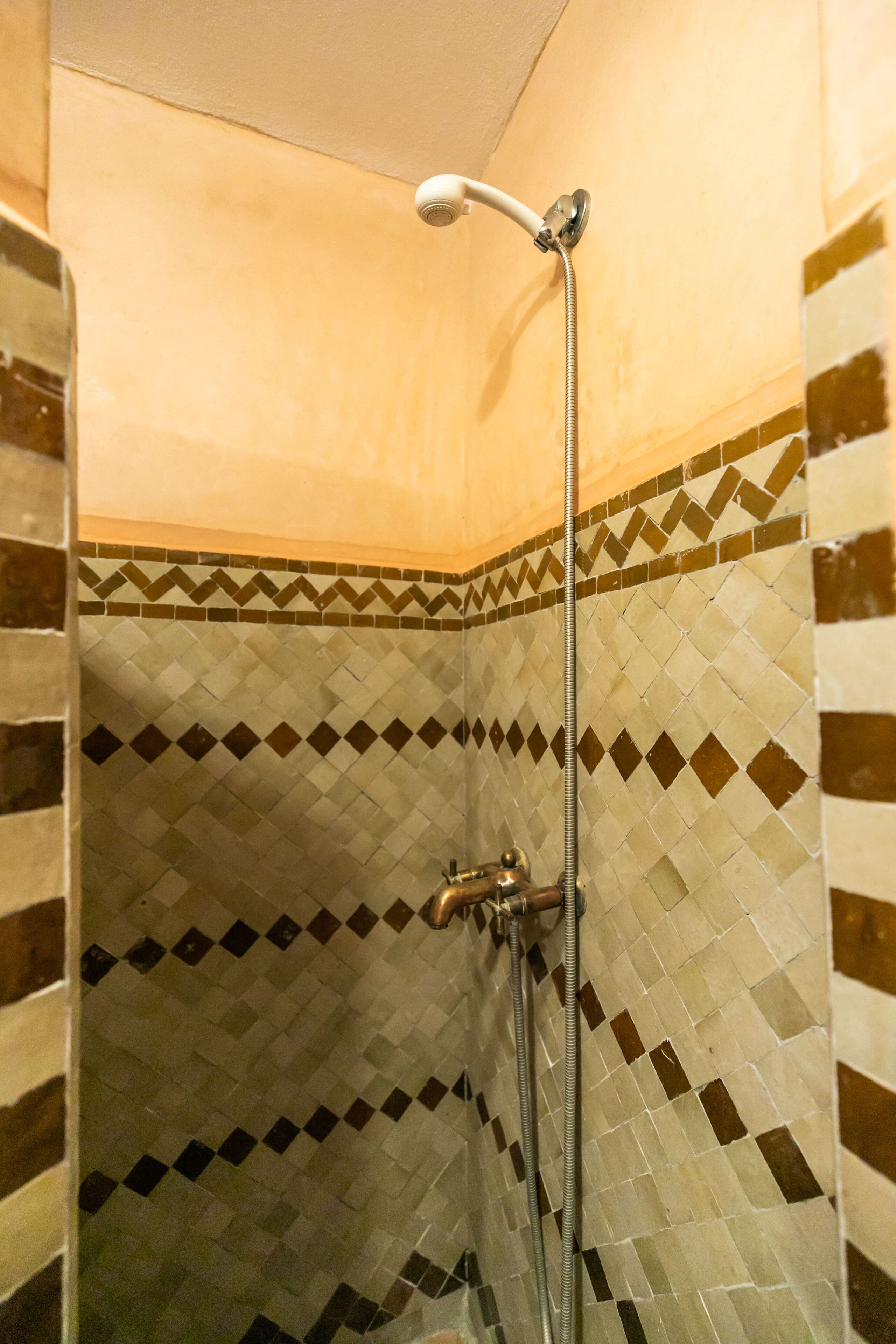 Ducha con cabezal de ducha manual y grifo empotrado. El área de la ducha tiene suelo y paredes con un patrón de diamantes.