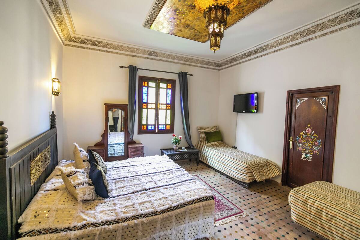 A room with a large bed, two smaller beds, a television, and a decorative door.