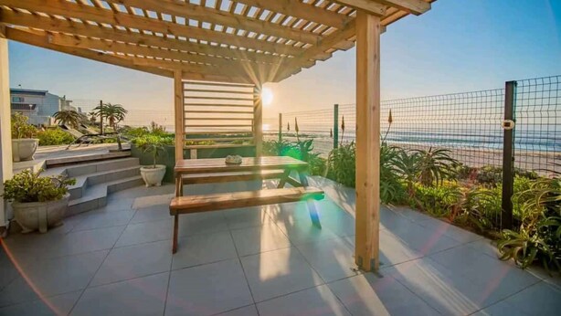 A covered outdoor area with a pergola, seating, and potted plants.