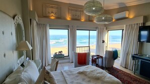 Quarto de hotel com cama, escrivaninha, cadeira, televisão e vista para a praia.
