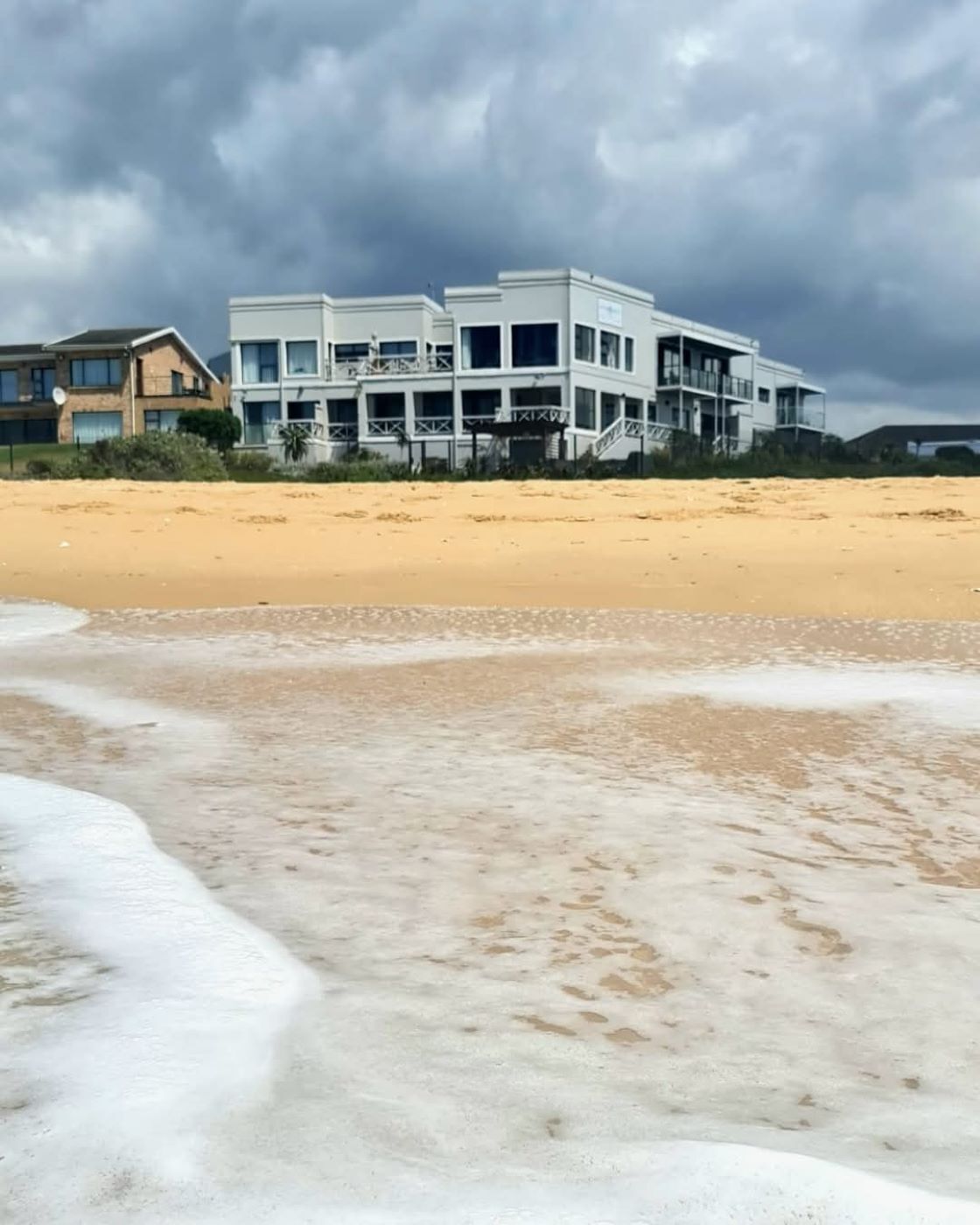 Ein Strandgrundstück mit einem mehrstöckigen Gebäude, Sandstrand und ankommenden Wellen.