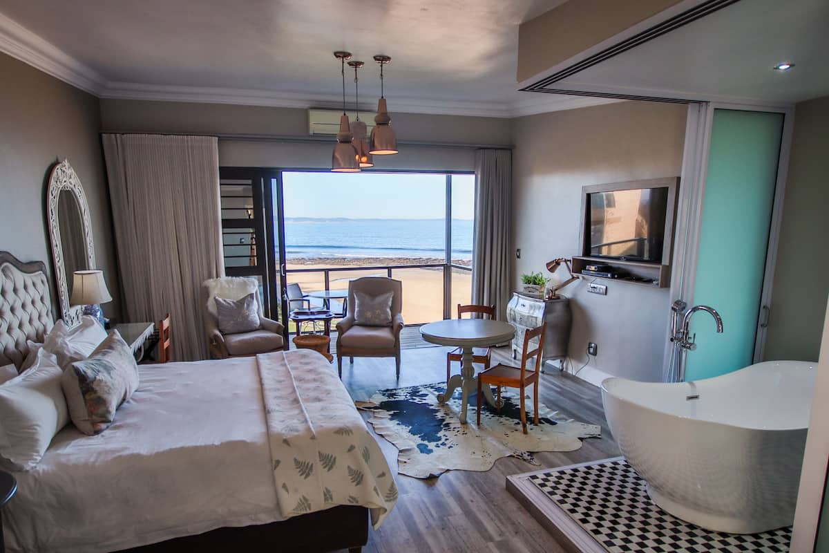 Une chambre d’hôtel avec un grand lit, un coin salon donnant sur la plage, une baignoire et un téléviseur.