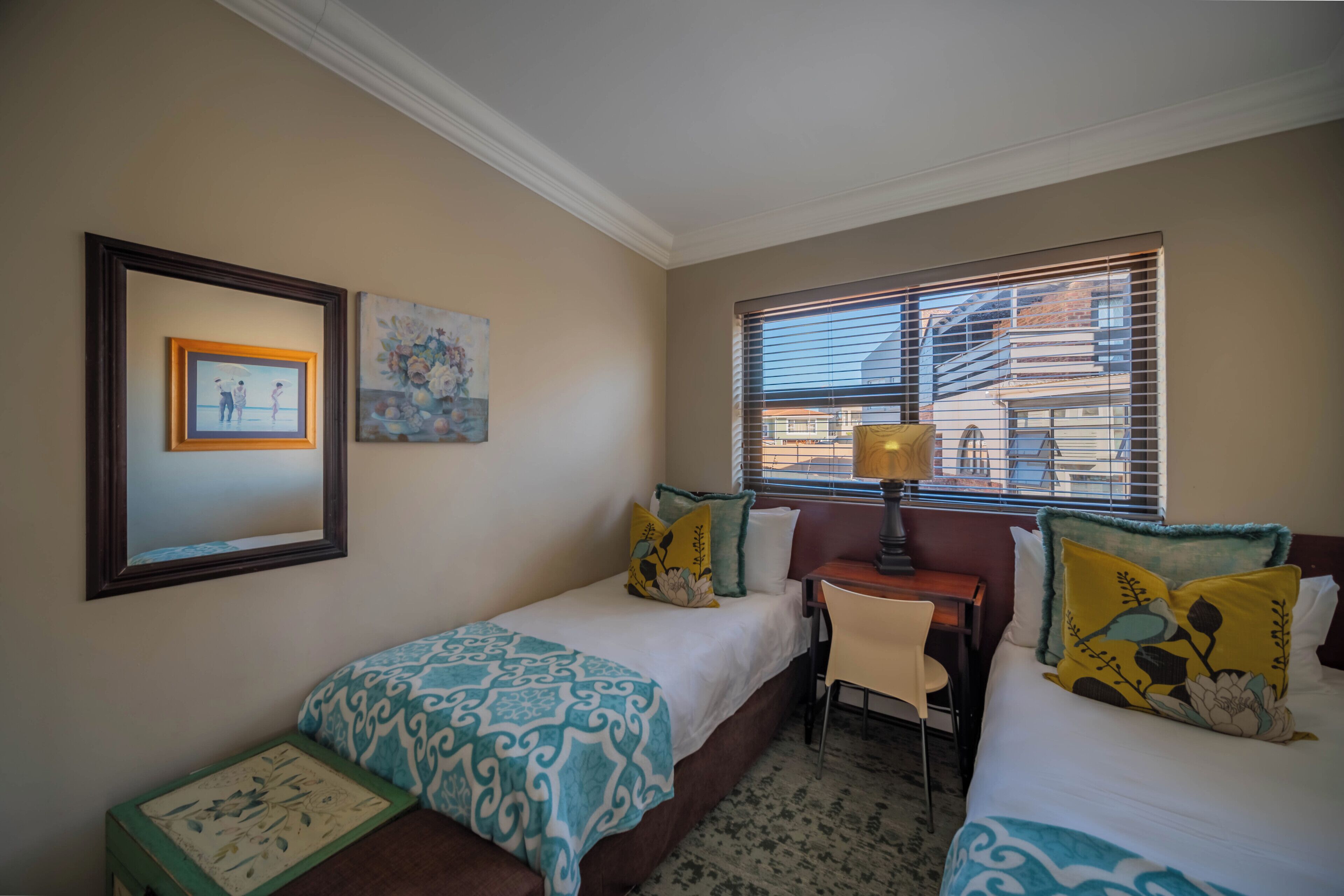 A hotel room with two beds, a desk, a chair, and a window with blinds.