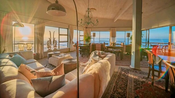 Uma sala de estar espaçosa com um sofá grande, uma mesa de jantar e vista para o mar.