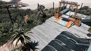 Um resort à beira-mar com um deque de madeira, espreguiçadeiras e uma placa com a inscrição 'THIS IS LIVING'.
