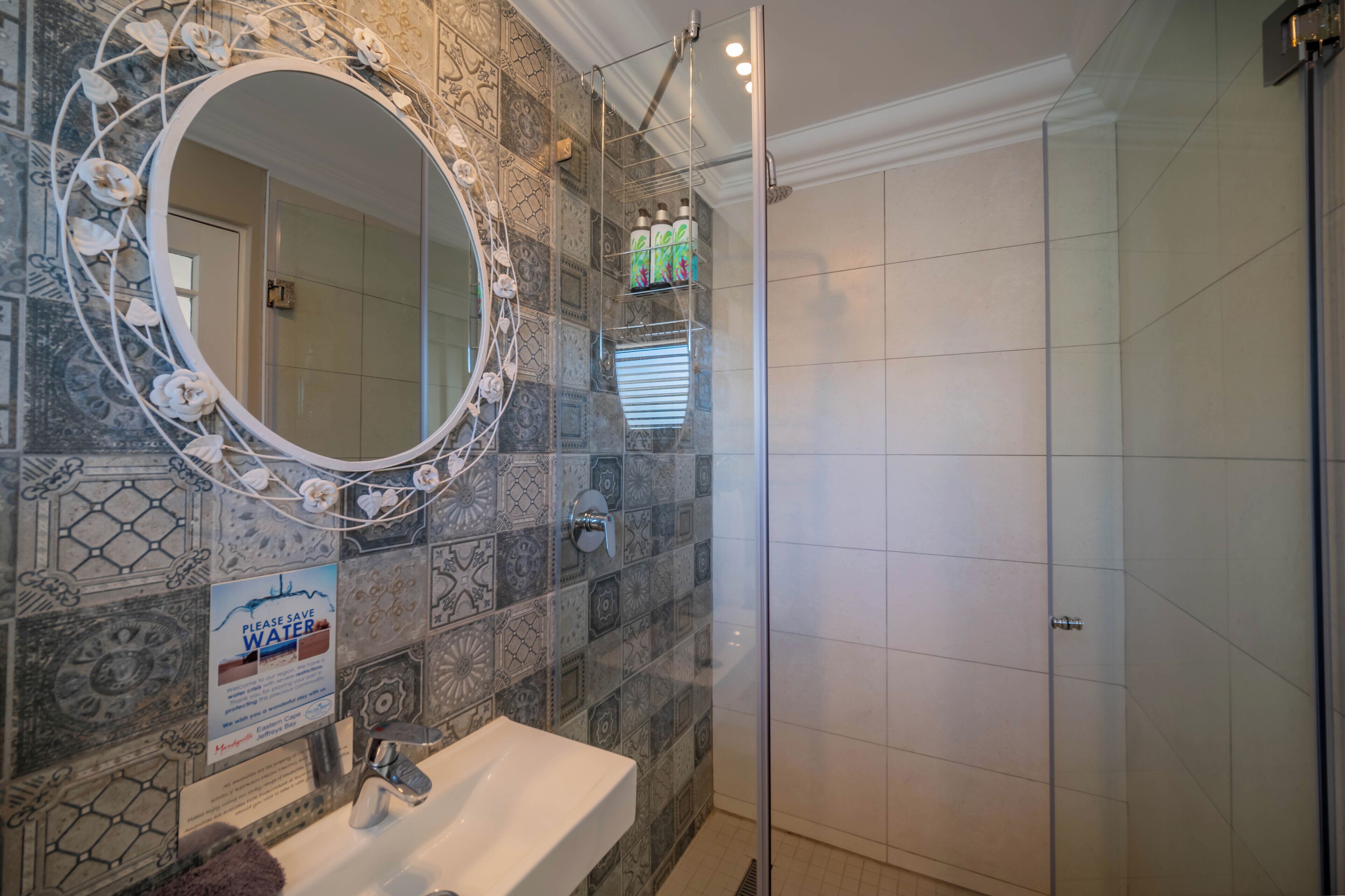 A bathroom with a sink, mirror, shower, and decorative tiles.