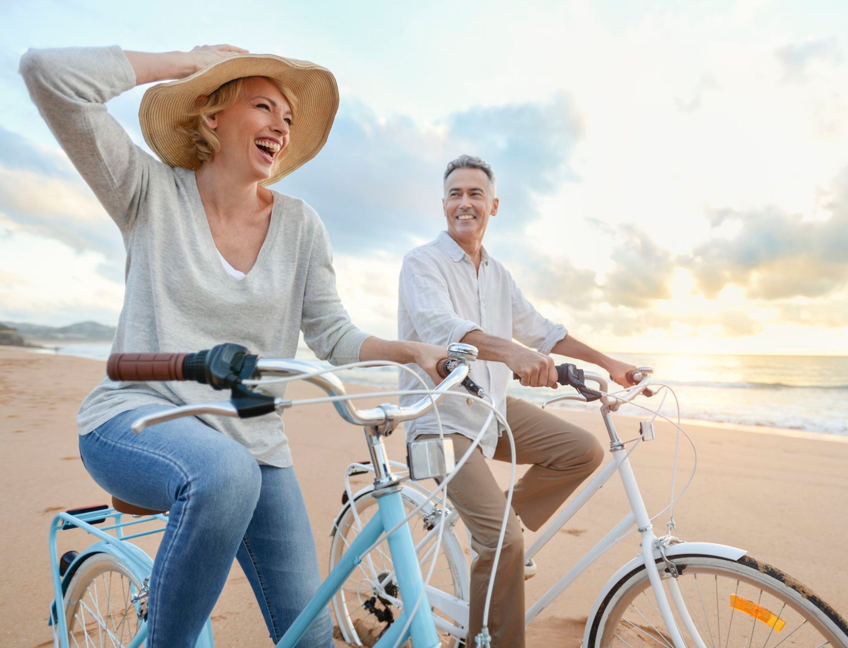 Two people riding bicycles on a beach with a sunset in the background.