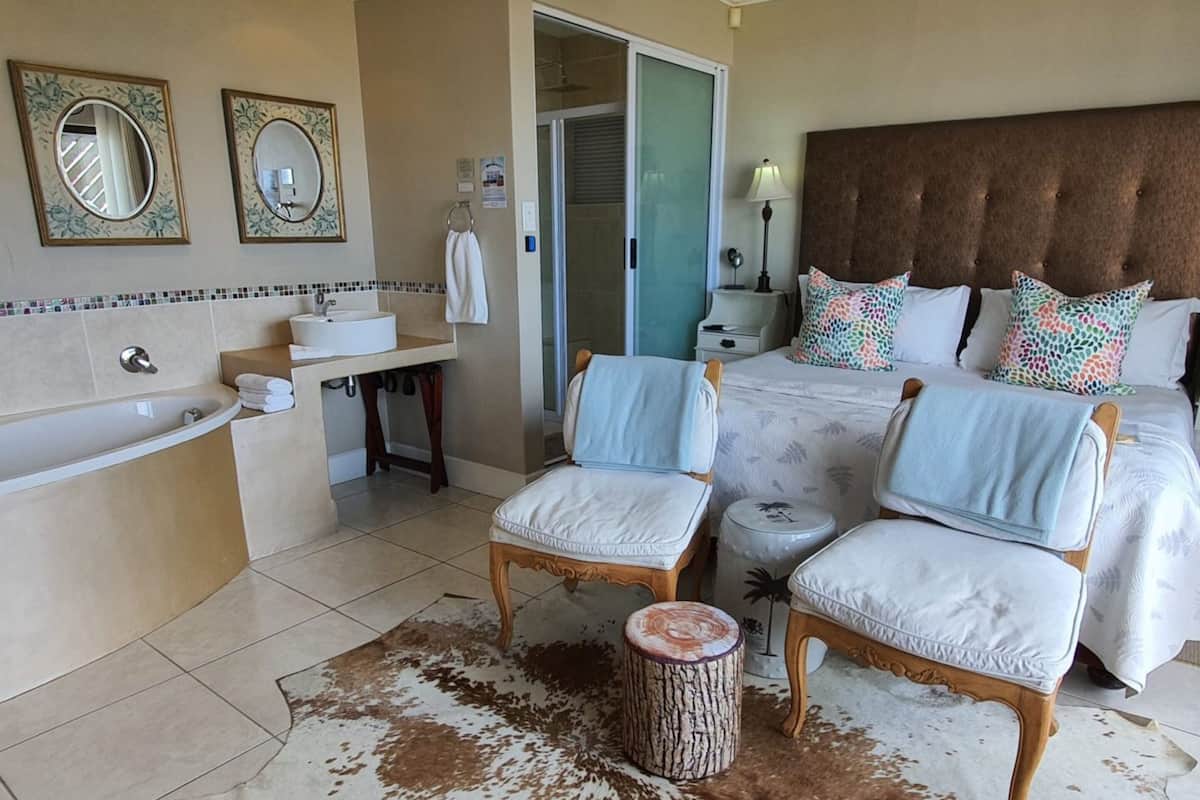 Une chambre d’hôtel avec un grand lit, deux chaises, une petite table, une baignoire et un espace douche.