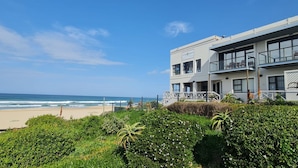 Um hotel moderno com varanda com vista para a praia, uma visão clara do oceano e um jardim bem cuidado em primeiro plano.