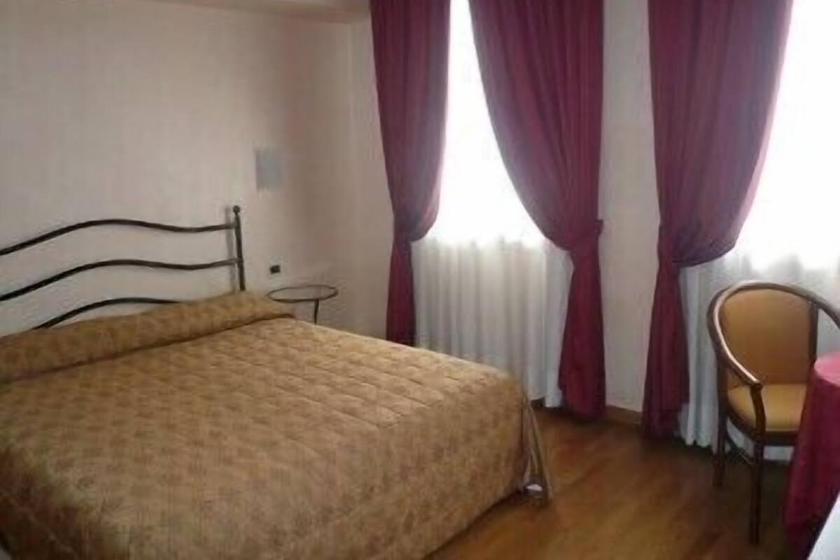 Een slaapkamer met een bed, een stoel, een tafeltje en een raam met gordijnen.