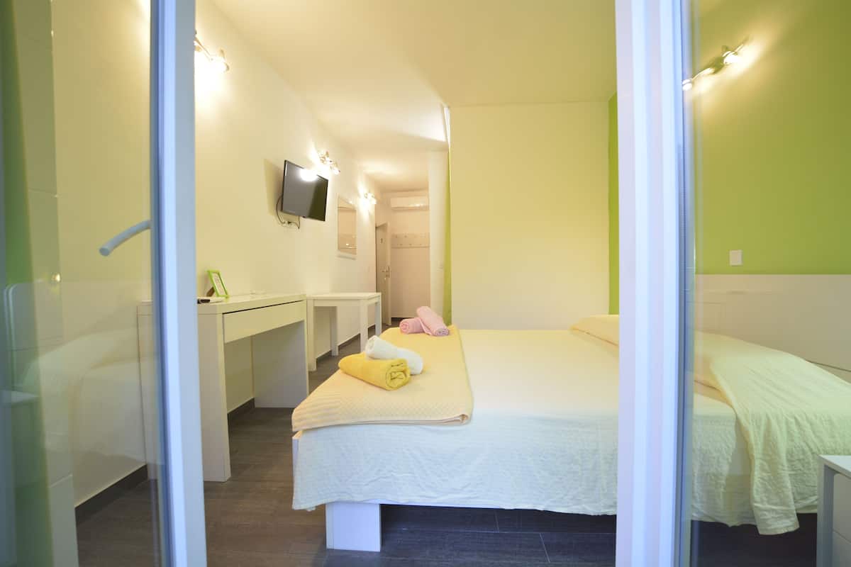 A hotel room with a bed, a desk, a chair, a TV mounted on the wall, and a bathroom visible through an open door.